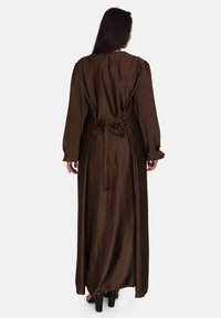 Lang bruin satijnen jurk met lange mouwen, gestrikt in de taille. Glad textuur, enkel-lang, met een eenvoudige ronde halslijn en vloeiende ontwerp.