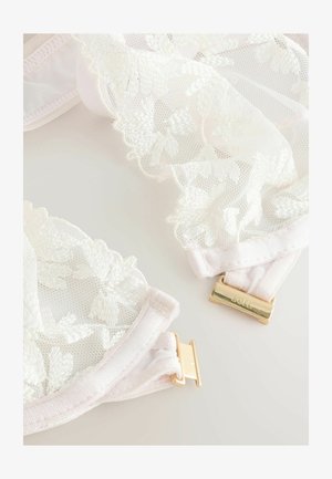 Brassière en dentelle avec un tissu doux et transparent en rose clair, ornée de broderies florales et de détails en métal doré sur les bretelles réglables.