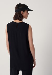 Ärm Solutions black top utan ärmar med en subtilt böjd nederkant, med en liten nyckelhålsskärning bak. En texturerad svart visir kompletterar looken.