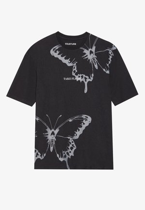 Svart t-skjorte med korte ermer laget av bomull, med store sølvfargede sommerfuglgrafikker og teksten "TAKE FLIGHT" i fet skrift.