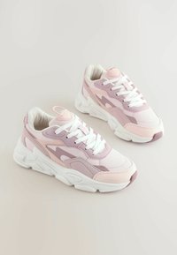 Adidași roz deschis și albi cu un design în straturi, panouri texturate și tălpi albe groase. Prezintă șireturi albe și un mâner pe călcâi.