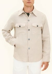 Lys beige, knap-op skjorte lavet af tekstureret stof. Har en krave, to brystlommer og blå knapper. Langærmede med en afslappet pasform.