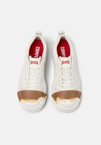 Sneakers bianche con tomaia in tessuto teksturizzato, intersuola in gomma e punta in gomma marrone con effetto sfumato. Soletta rossa con logo "CAMPER".