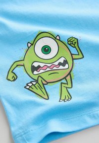 Lyseblå bomulds T-shirt med et grønt tegneseriemonster med et stort øje, udtryksfuld mund og hævede arme.