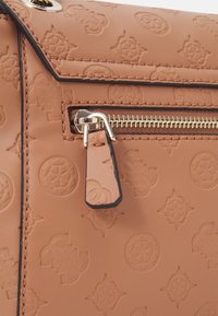 Světle hnědá kožená taška s reliéfním vzorem, vybavená kapsou na zip a kovovým zipem. Okraje jsou ohraničeny tmavším lemováním.