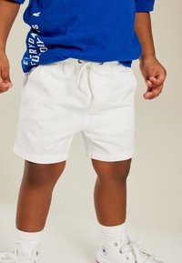 White cotton shorts with elastic waistband and drawstring. Paired with blue long-sleeve shirt and white high-top sneakers.