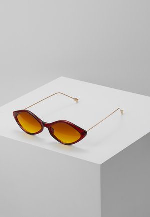 Gafas de sol de ojo de gato con montura burdeos, lentes amarillos degradados y delgadas varillas de metal dorado, con puntas puntiagudas y curvas suaves.