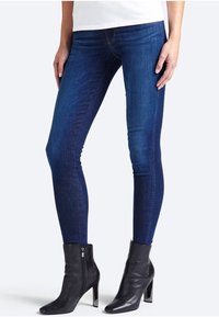 Jeans ajustados en denim de un azul oscuro, con una cintura alta, detalles de costura sutiles, combinados con botas de tobillo negras con cremallera.