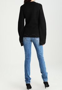 Suéter de punto negro con mangas largas y dobladillo en forma de concha, combinado con jeans de mezclilla azul claro y zapatos de tacón negros.