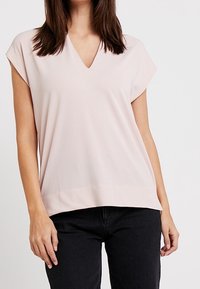 Ljust rosa blus med V-ringning, korta ärmar och en avslappnad passform. Slät textur och en jämn fåll kompletterar svarta byxor.