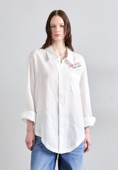 Chemise en lin blanche à boutons avec un ourlet arrondi et une poche poitrine. Présente un texte brodé coloré sur l'épaule gauche.