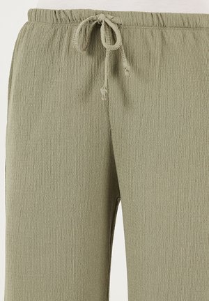 Gaiši zaļi, teksturēti bikses ar elastīgu jostu un auklas aizdari. Iezīmē brīvu piegriezumu un mazu sašaurinājumu pie potītēm.