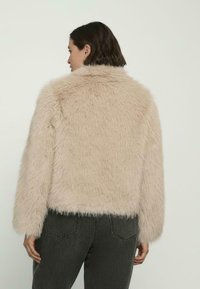 Kurtka z futerka ekologicznego w beżowym kolorze o puszystej fakturze. Posiada wysoki kołnierz i długie rękawy, kończące się na wysokości talii prostym cięciem.