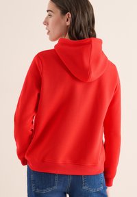 Sudadera roja con una textura suave, que cuenta con una capucha grande y puños acanalados. La parte trasera presenta un acabado suave y un diseño sencillo.