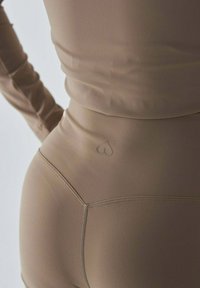 Brązowe dopasowane legginsy o gładkiej fakturze, z małym serduszkiem na tylnej części pasa oraz bezszwowymi szwami.