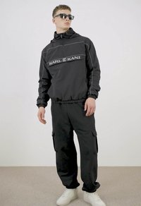 Black hoodie with a front pocket and reflective stitching, paired with loose black cargo pants featuring side pockets and white sneakers.