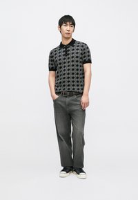 Čierno-biely vzorovaný polo s krátkym rukávom a golierom, kombinovaný so sivými džínsami so strihom na rovné nohy a čiernymi teniskami. Nový detail textúrovaného dizajnu.