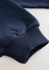 Tissu de sweat-shirt bleu marine avec une surface lisse et des poignets en côtes. Les poignets sont tissés serrés et élastiques pour un ajustement parfait.
