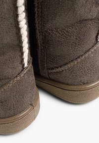 Botas de tobillo de ante marrón con un acabado texturizado, que cuentan con una cremallera lateral y costuras blancas contrastantes. Las suelas de goma ofrecen agarre y durabilidad.