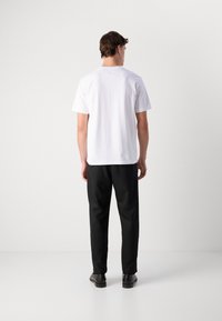 T-shirt blanche à manches courtes avec un col rond, associée à un pantalon noir et des chaussures noires ; design minimal avec aucun motif ou logo visible.