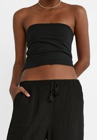 Zwarte bandeau top van rekbare stof, nauwsluitend ontwerp met een gladde textuur. Gecombineerd met zwarte broek met textuur, zijzakken en trekkoord.