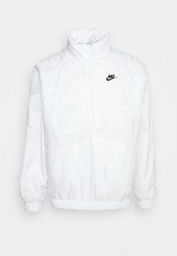Vit Nike-pulloverjacka med hög krage, 1/4 zip-stängning, elastiska ärmslut och midja. Har en liten svart logotyp på bröstet.