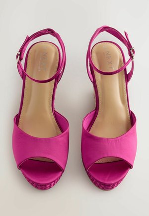 Lysende pink højhælede sandaler med åben tå og ankelrem, der har en vævet tekstur på plateauet, præsenteret mod en neutral baggrund.
