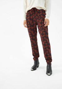 Schwarze Hose mit einem roten Blumenmuster, ausgestattet mit einem elastischen Taillenbund und Bündchen. Getragen mit schwarzen, spitzen Ankle Boots.