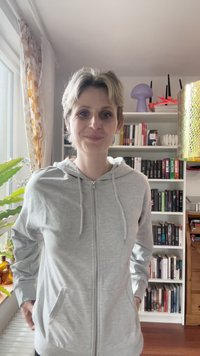Haut de sweat à capuche zippé gris clair avec cordon de serrage, poches avant et tissu lisse et texturé, porté sur un pantalon noir.
