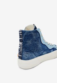 Vysoké tenisky s vybledlým modrým denimovým svrškem, světle modrými semišovými detaily, bílými tkaničkami a silnou bílou gumovou podrážkou, nakloněné tak, aby ukázaly zadní a boční stranu.