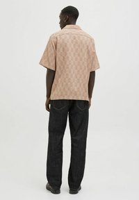Chemise à manches courtes en tissu rose clair texturé avec un motif en chevrons, associée à un jean en denim foncé. Design de col simple.