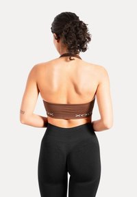 Brązowy prążkowany krótki top z wysokim dekoltem i regulowanymi ramiączkami, zestawiony z wysokim stanem czarnych legginsów o gładkiej fakturze.