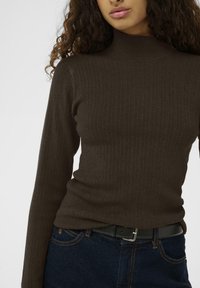 Maglione a collo alto a coste marrone con maniche lunghe, presenta un design aderente. Abbinato a jeans in denim scuri e a una cintura nera.