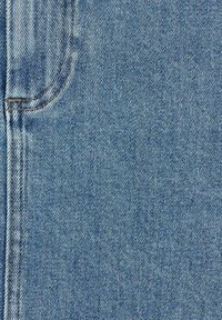 Gros plan sur un tissu en denim bleu montrant des coutures détaillées et un bord de poche courbé avec des coutures visibles.