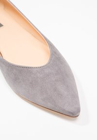 Grå mocka ballerina med spetsig tå och låg klack, med en slät, mjuk känsla och en enkel design.