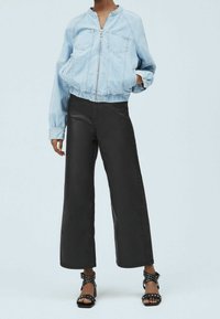 Chaqueta de mezclilla corta en azul claro con cremallera frontal y dos bolsillos en el pecho, combinada con pantalones de pierna ancha negros de cintura alta y sandalias negras de tacón.