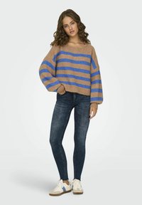 Maglione a righe marroni e blu con vestibilità rilassata e maniche a palloncino, abbinato a jeans skinny scuri e sneakers chiare.