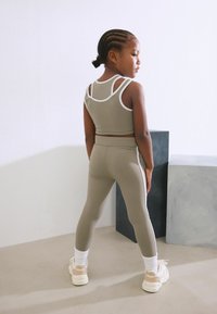 Ensemble de sport de couleur marron clair comprenant un top cropped avec des accents blancs et un legging assorti. Matériau texturé avec un design sportif et une coupe adaptée.