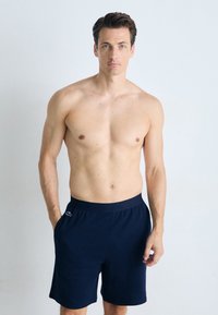 Pantalones cortos azul marino con cinturilla elástica y acento del logo de Lacoste. La tela parece suave y ligera, diseñada para la comodidad y la facilidad de movimiento.