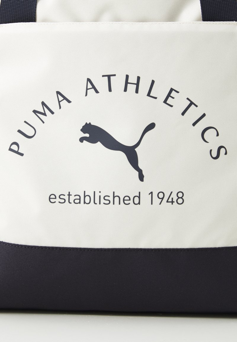 Borsa in tessuto bianco con dettagli neri, caratterizzata dal testo "PUMA ATHLETICS" e dal logo del Puma saltante. Il testo recita "fondato nel 1948".