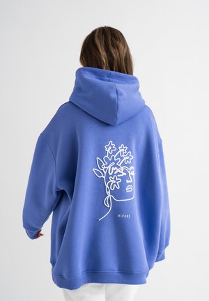 Overmaatse blauwe hoodie van zachte stof, met een witte lijntekening van een gezicht en bloemen op de achterkant. Met capuchon en geribde boorden.