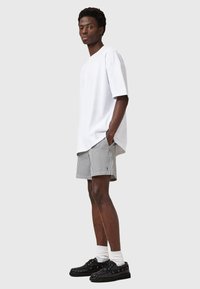 Maglietta bianca oversize, pantaloni corti a righe, scarpe da ginnastica nere e calzini bianchi. Design semplice, vestibilità rilassata, colori a contrasto e tessuto leggero.