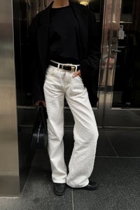 Biele textúrované široké nohavice, čierny priliehavý top, prehnaná čierna blazer a čierna kabelka so zipsom. Zlatá pracka na opasku pridáva kontrast.