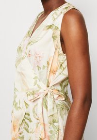 Bloemjurk in roomkleur met roze en groene patronen, met een diepe V-hals, mouwloos ontwerp en een strikaccent op de taille.