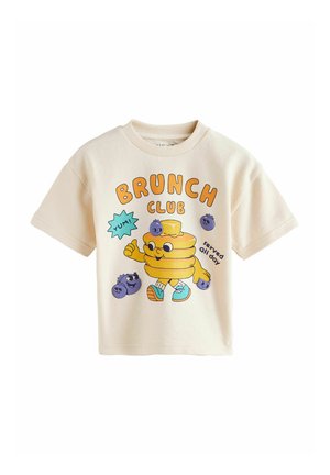 Beige kortærmet toddler-skjorte med tegneseriepandekager iført sneakers, blåbær og tekst "BRUNCH CLUB serveret hele dagen" og "YUM!"