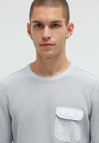 Graues, strukturiertes Langarmshirt mit rundem Ausschnitt und einer kleinen Brusttasche. Verfügt über ein gewebtes Muster und kontrastierende Taschendetails.