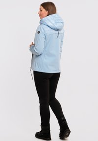 Lysblå, pufjet jakke med hætte, lynlåslommer og sorte detaljer. Båret over sorte leggings og støvler, hvilket fremhæver den tætsiddende design.