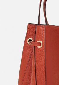 Rostfärgad läderhandväska med en texturerad yta, som har en detalj med guldfärgade ögla och en strukturerad, vinkelräffad form.