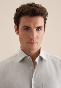 Lys grå skjorte med knaplukning og lille krave, diskret tekstur, frontlomme og hvide knapper. Glat, letvægtsstof.