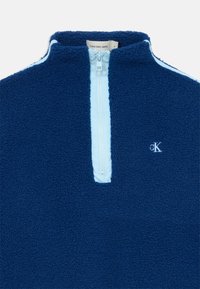 Pullover in pile blu con zip e dettagli del colletto azzurri. Presenta una zip frontale e un logo ricamato sul petto. Texture morbida.